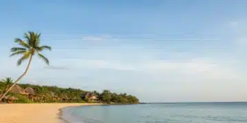 Serene beach during off-peak season, calm ocean, clear sky, symbolizing travel savings.