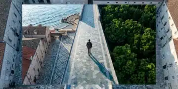 Aerial view of a person walking on a geometrically patterned city square, transitioning to a coastline and forest, representing diverse travel choices for beginners.